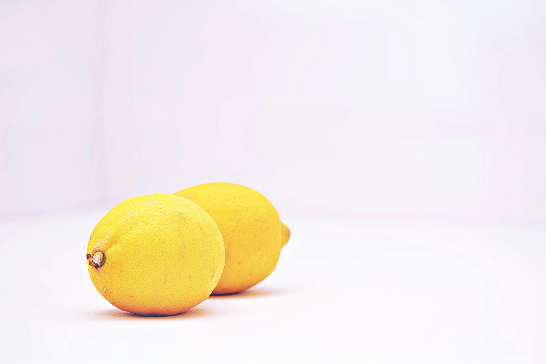 Hand with white nails holding a fresh lemon on soft pink background with additional lemons nearby