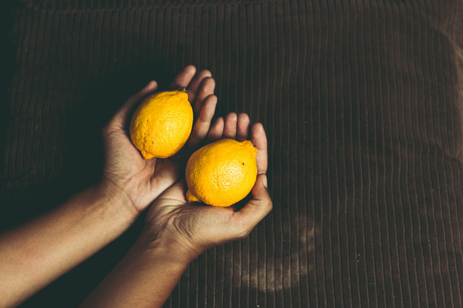 Close-up of hands holding fresh lemons on a brown surface, symbolizing freshness and natural support