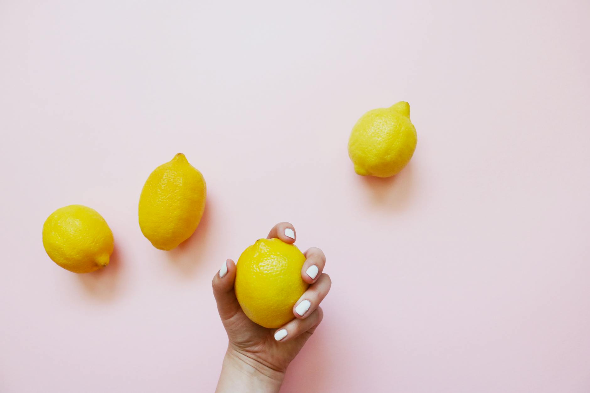 A hand holding a fresh lemon on a soft pink background, symbolizing the subtle power of lemon vibrators
