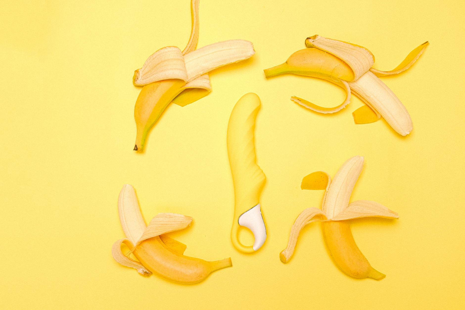 Yellow silicone lemon vibrator surrounded by fresh lemons on bright yellow background