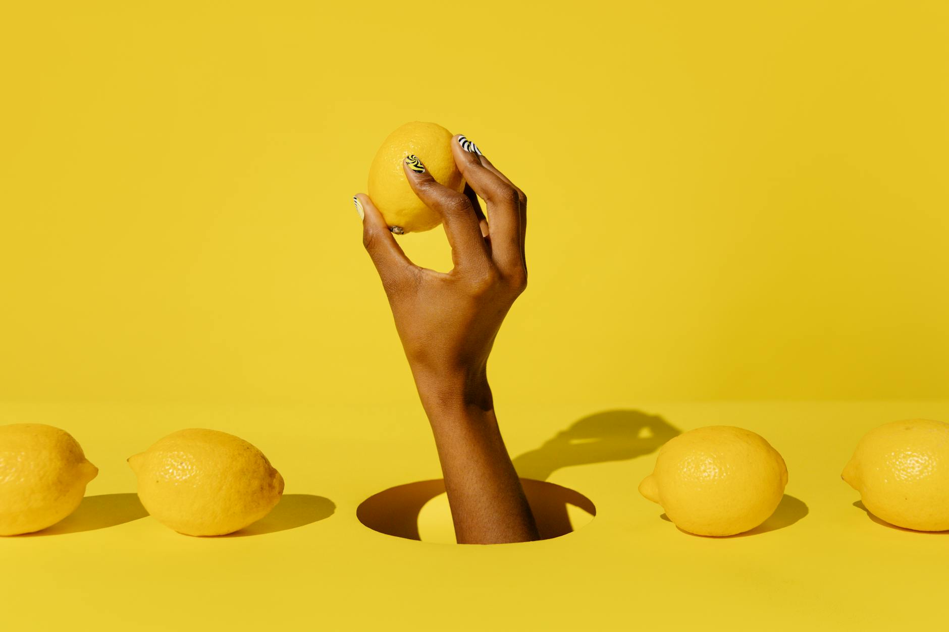 Hand holding a fresh lemon on bright yellow background, symbolizing renewal and sensual pleasure