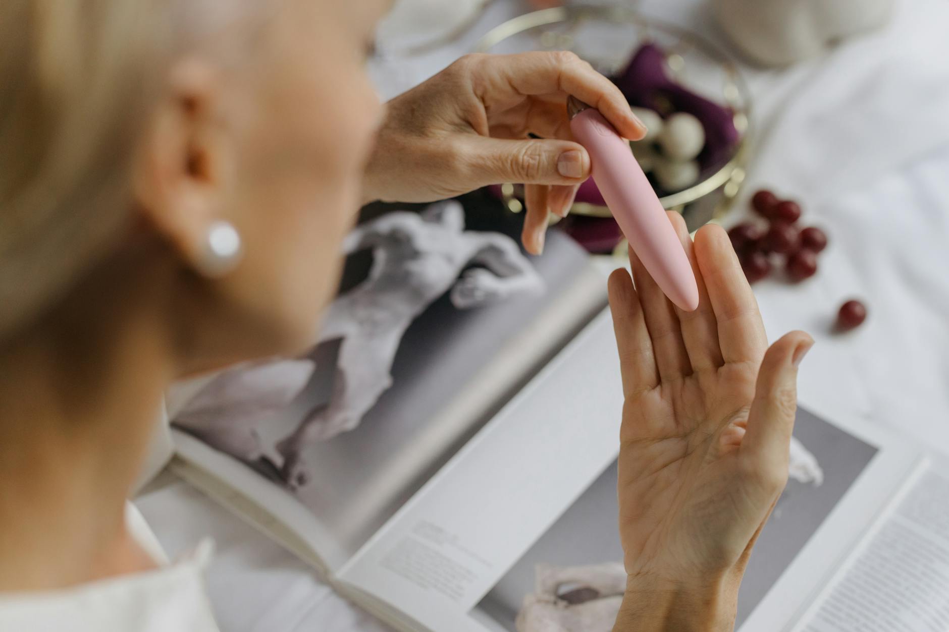 Close-up of hands holding a pink vibrator with art books nearby, emphasizing intimate personal wellness