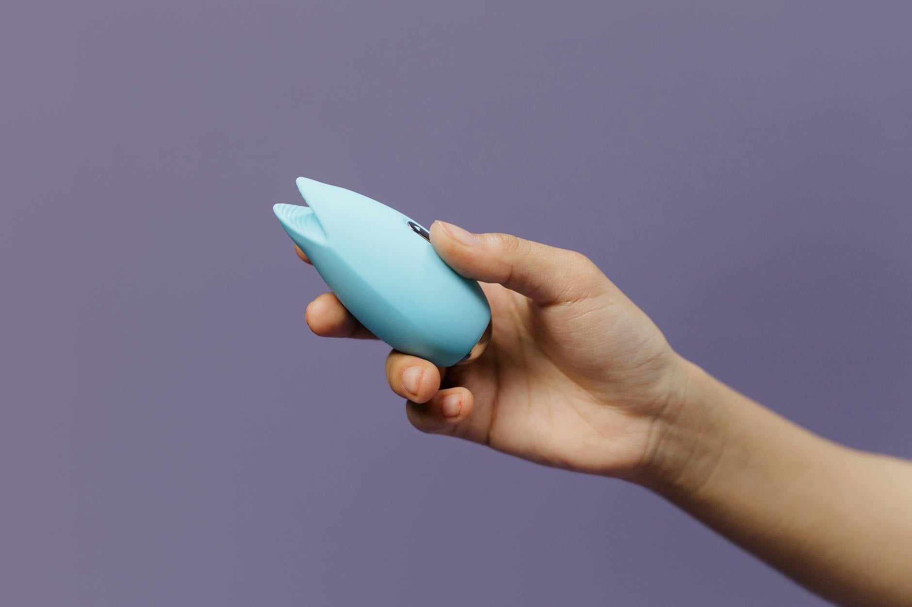 A lemon clitoral vibrator held in hand against a solid purple background, showing its compact design for sensitive touch