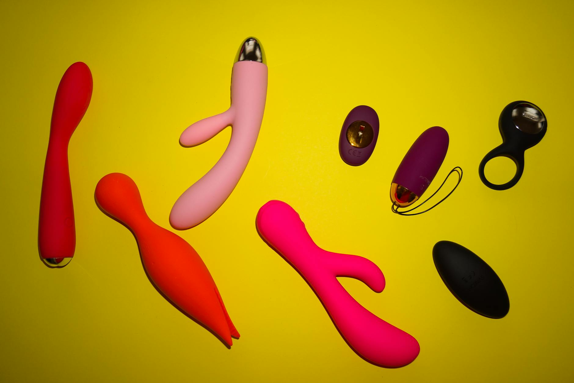Vibrant collection of colorful clitoral vibrators and pleasure toys arranged on a bright yellow surface