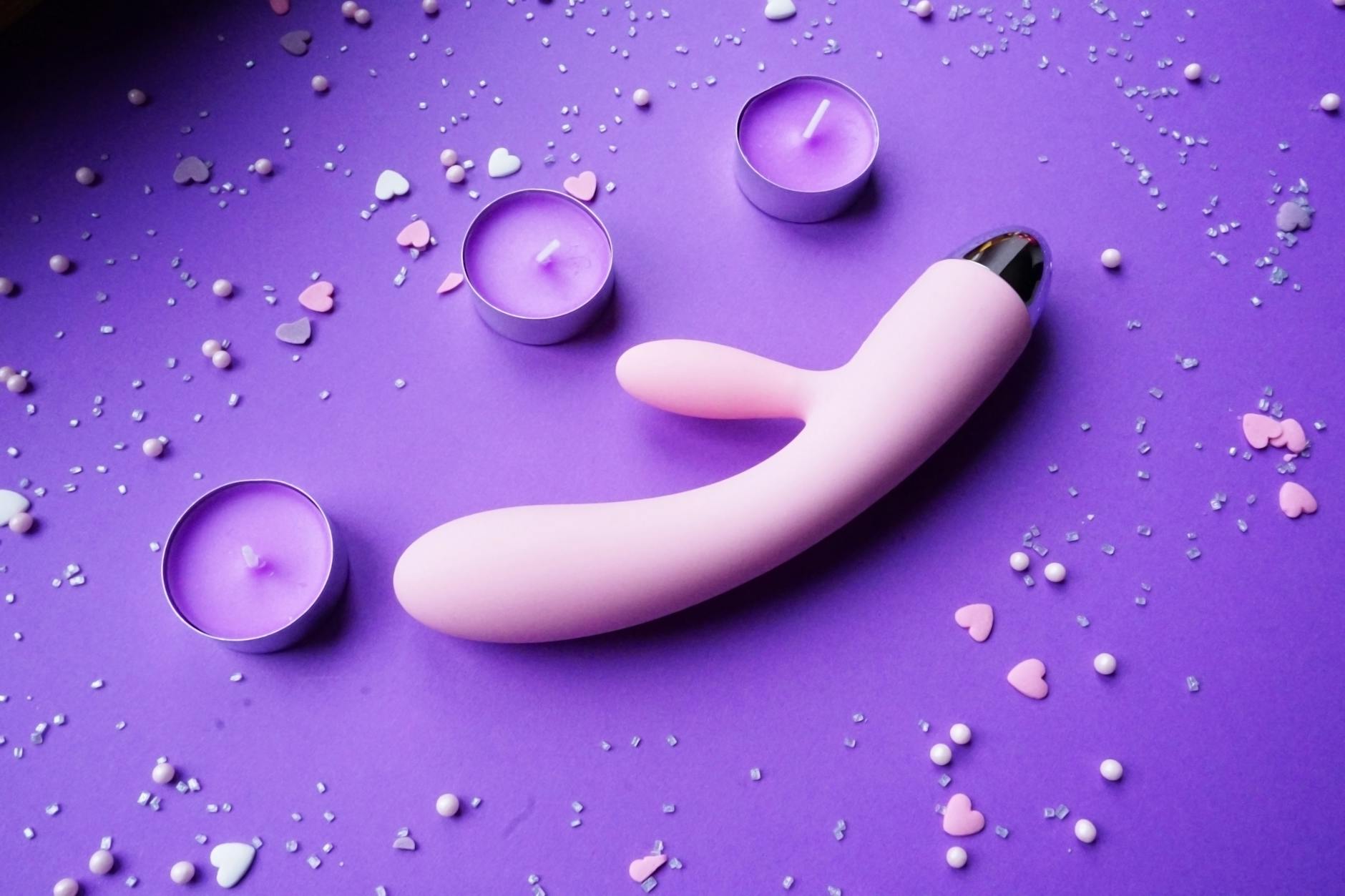 Pink vibrator on purple background with heart confetti and candles for romantic reconnection